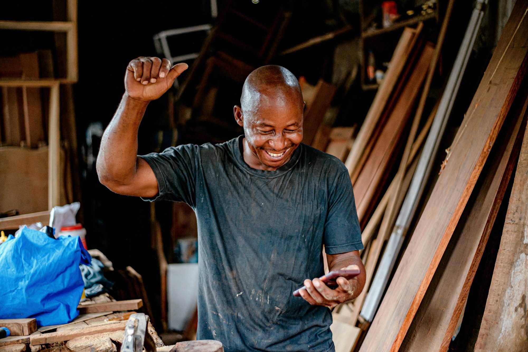 A carpenter in his workshop smiling at a message on his phone